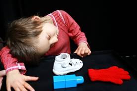 The girl Zinka is playing with a white shoe, a red glove and a blue cube on a black background.